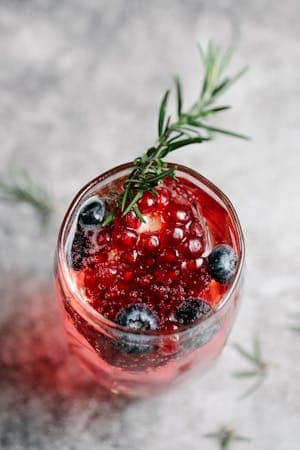 A refreshing berry cocktail with blueberries and rosemary, served in a glass.