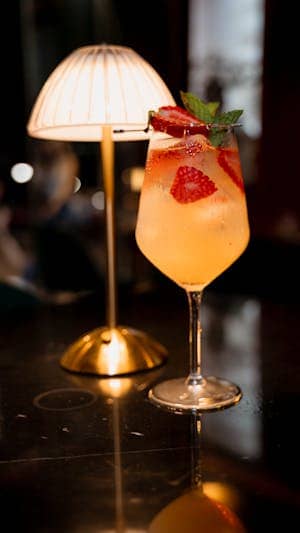 A refreshing strawberry cocktail in a glass set against a warm-lit background indoors.