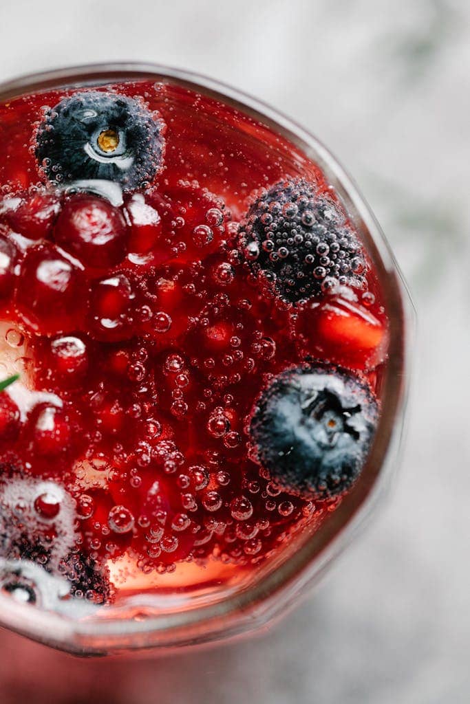 Top view of a bubbly red berry drink with blueberries and currants.
