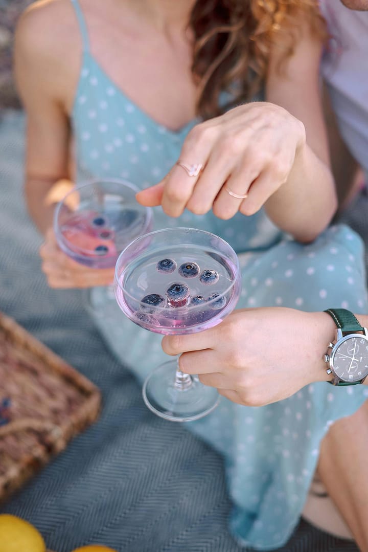 Elegant outdoor picnic featuring blueberry-infused mocktails in coupe glasses, set against a summer backdrop.